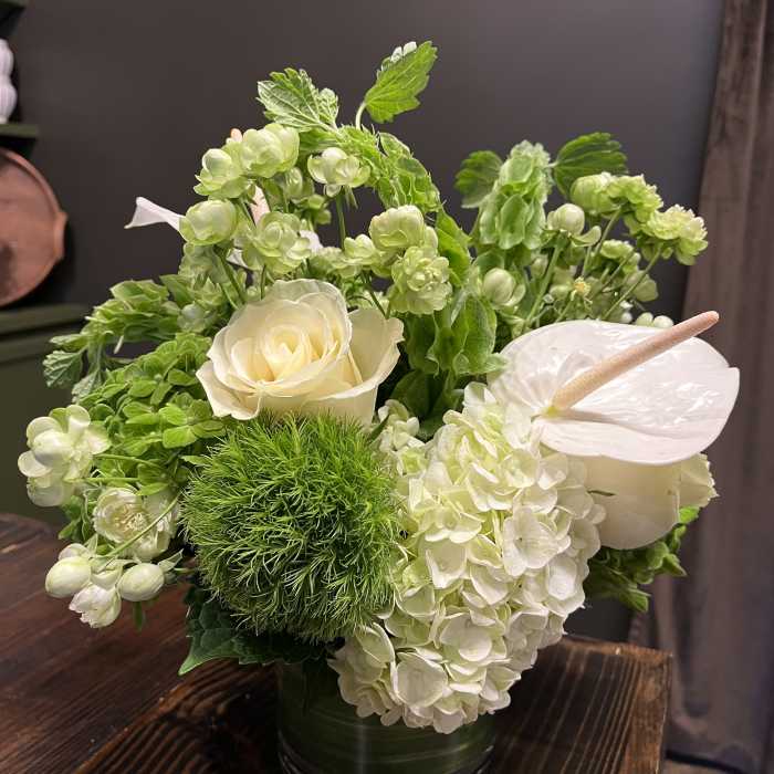 White roses and hydrangeas in a green vase with anthurium and green blooms