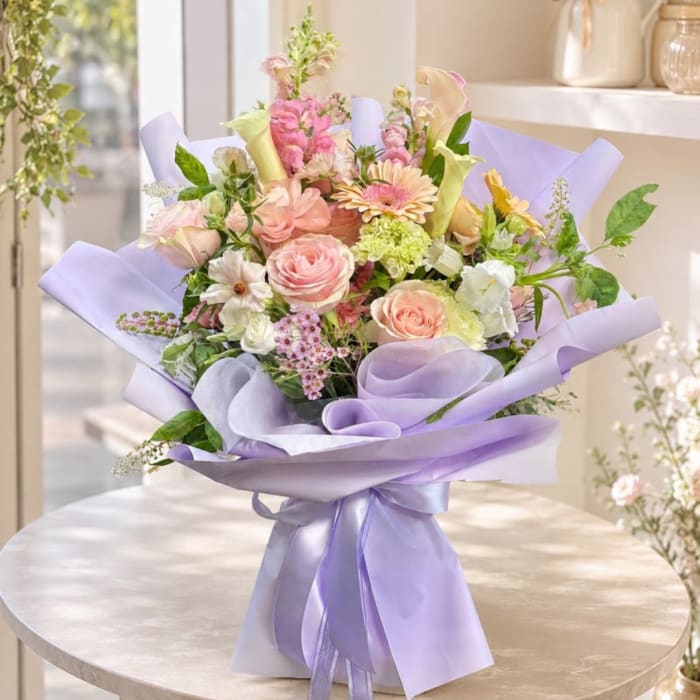Pastel bouquet of roses, calla lilies, and mixed blooms wrapped in lavender paper