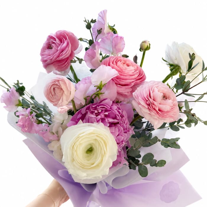 Handheld bouquet of pink, purple, and white ranunculus with lavender wrap