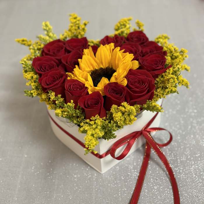 Heart-shaped box of red roses with a sunflower center and red ribbon