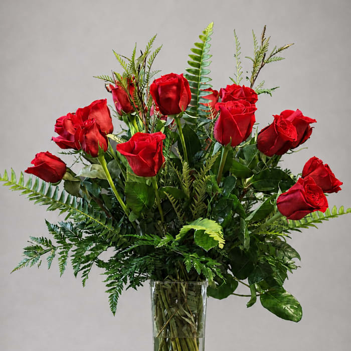 Red roses arranged in a clear glass vase with greenery
