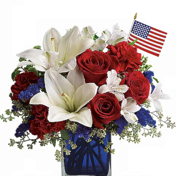 Red roses and white lilies in a blue glass vase with a small American flag