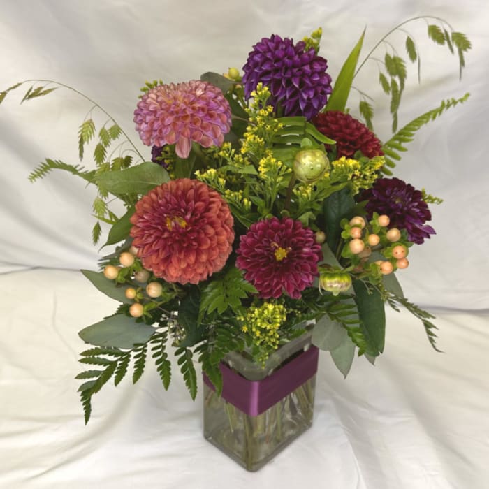 Mixed dahlia bouquet in a clear square vase with a purple ribbon