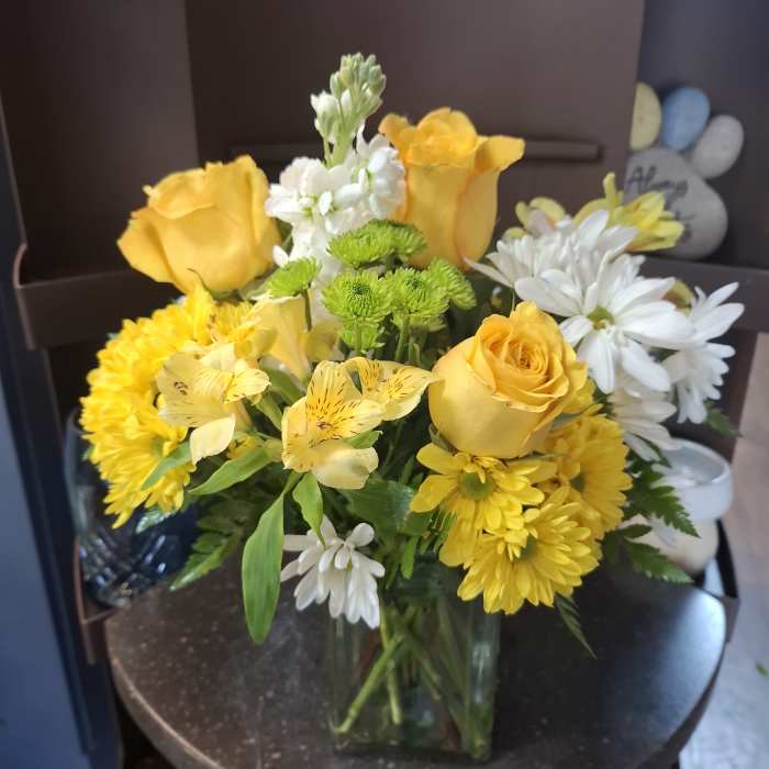 Yellow roses and white daisies arranged in a clear glass vase