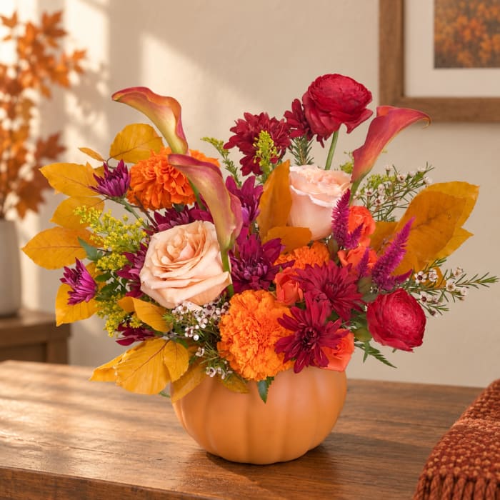 Autumn floral arrangement in a pumpkin-shaped vase with orange and red blooms