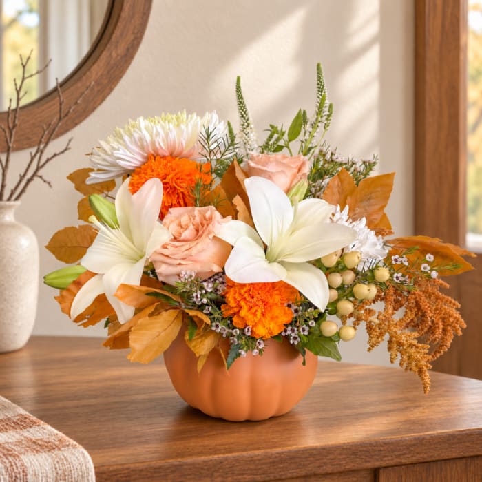 Autumn floral arrangement in a pumpkin-shaped vase with white lilies and orange blooms