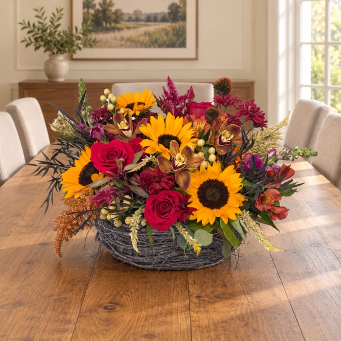 Mixed bouquet with sunflowers, red roses, and orchids in a gray basket