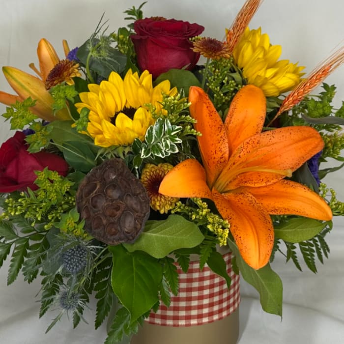 Mixed bouquet with orange lilies, red roses, and yellow sunflowers in a gingham-wrapped container.