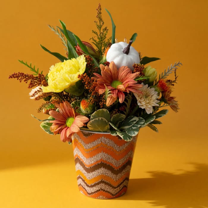 Autumn flower arrangement in a patterned orange pot with a white pumpkin accent