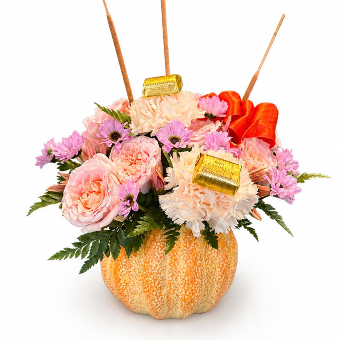 Pink and peach floral arrangement in a pumpkin container with chocolate bars