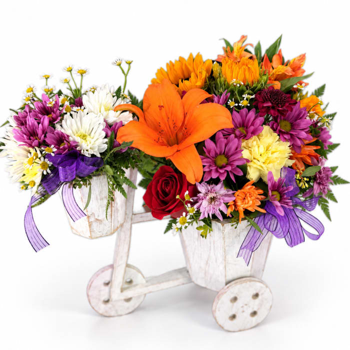 Two colorful flower arrangements in white wooden carts with purple ribbons