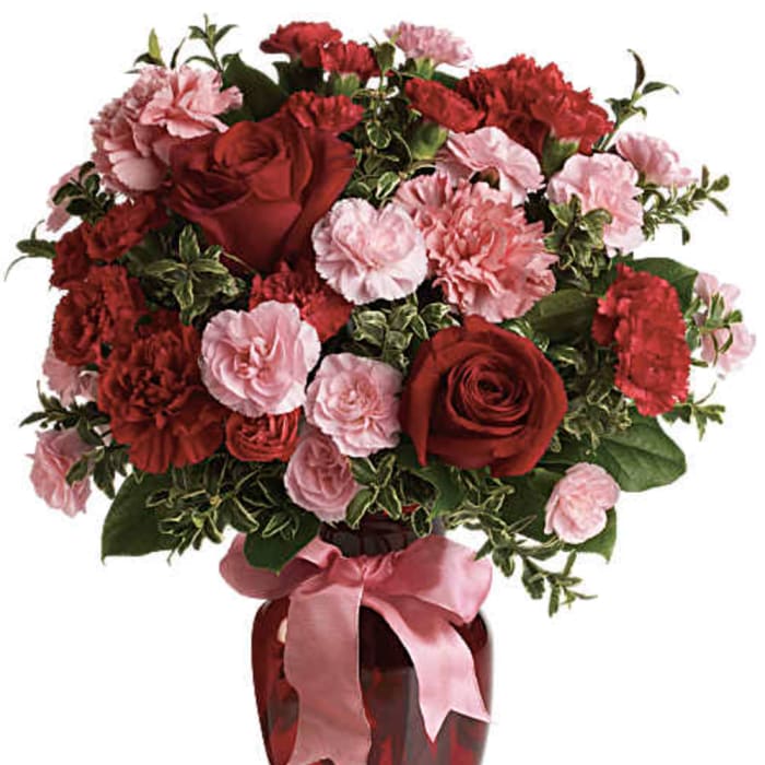 Red roses and pink carnations in a red vase with a pink ribbon