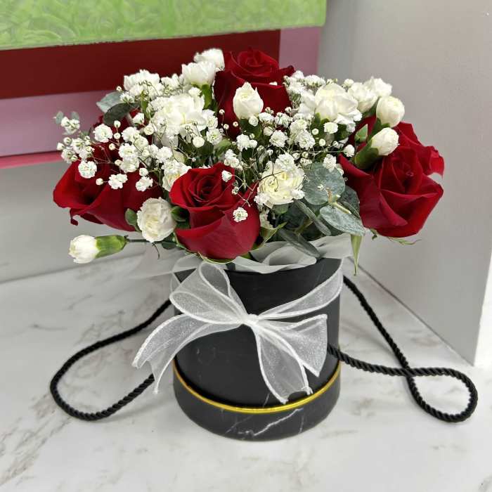 Red and white rose arrangement in a black round box with a white ribbon