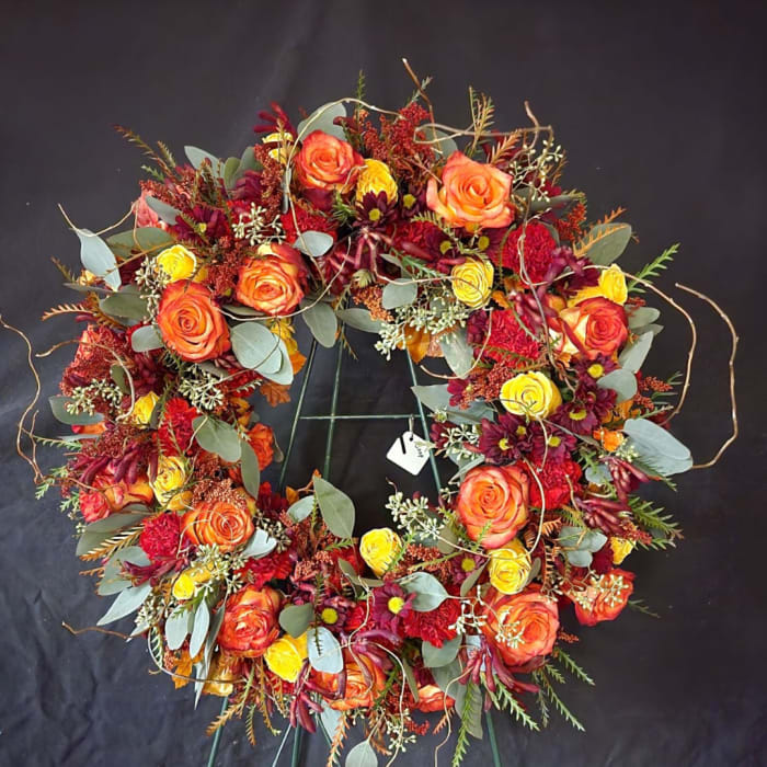 Circular floral wreath with orange and yellow roses on a black stand
