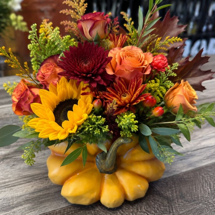 Fall floral arrangement in a pumpkin-shaped container with sunflowers and roses
