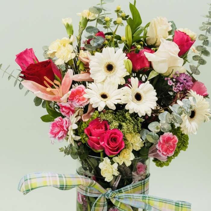 Mixed bouquet of pink and white flowers in a glass vase with a plaid ribbon