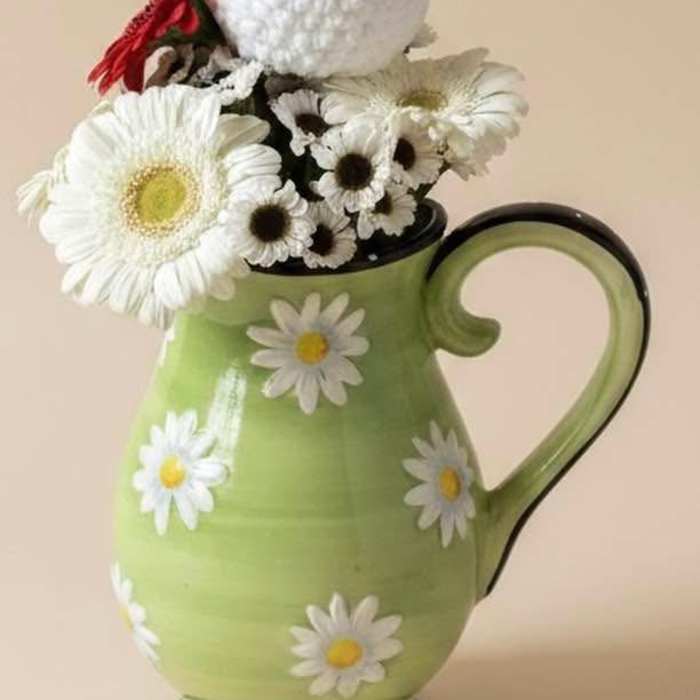 Daisy arrangement in a green pitcher with a crocheted chicken topper