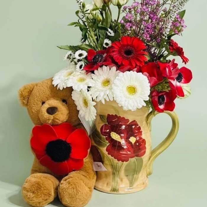 Bouquet in a floral mug beside a teddy bear with red flower accents