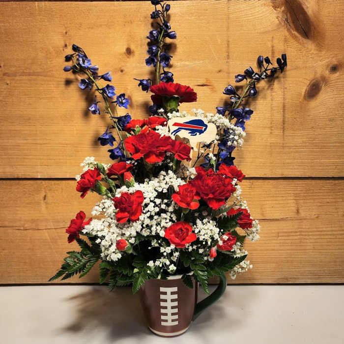 Red carnations and white filler flowers in a football mug with blue accents