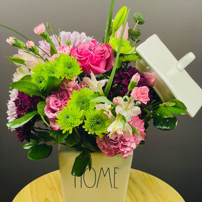 Pink and green mixed bouquet in a white container labeled HOME