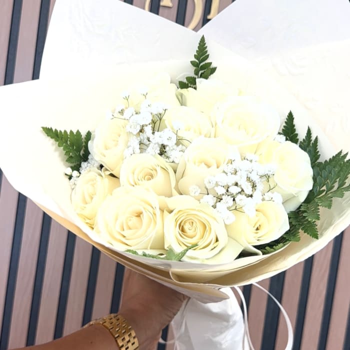 Bouquet of pale yellow roses with white filler flowers wrapped in white paper