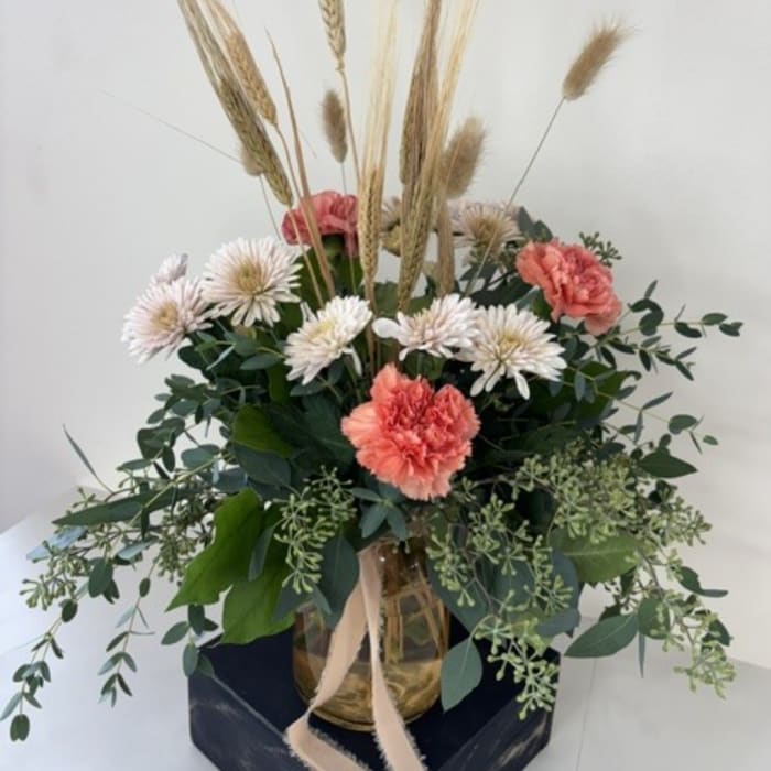 Arrangement of white daisies and coral carnations in a glass vase with dried grasses
