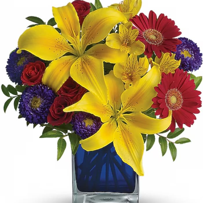 Yellow lilies, red roses, and purple daisies in a blue glass vase