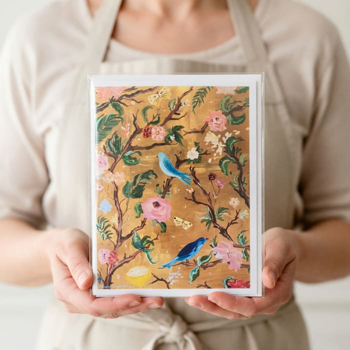 Person holding a floral greeting card with birds and blossoms