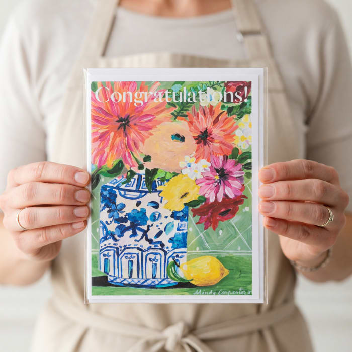 Person holding a floral congratulations card with a painted vase and flowers