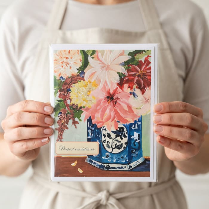 Person holding a condolence card with a floral painting and vase