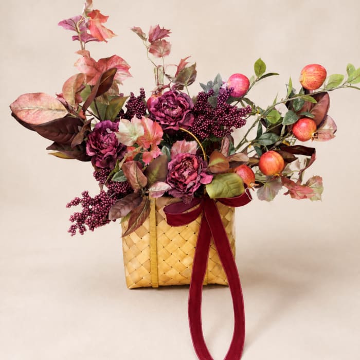 Autumn floral arrangement in a woven basket with burgundy ribbon