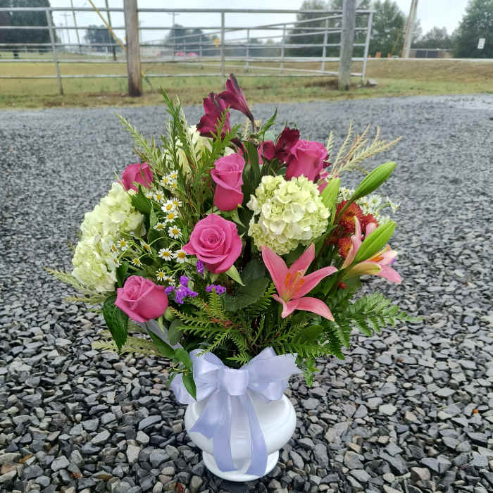 Pink roses and lilies arranged in a white vase with a lavender ribbon