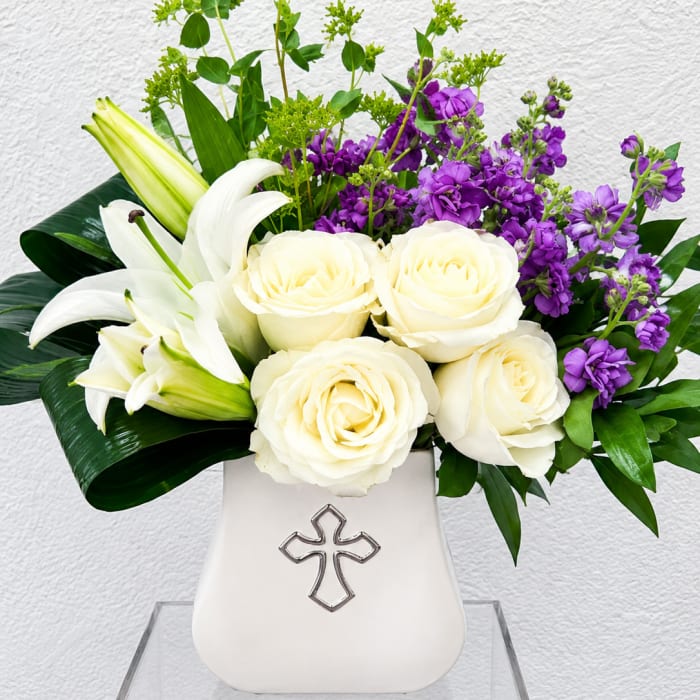 White roses and lilies arranged in a white vase with purple flowers