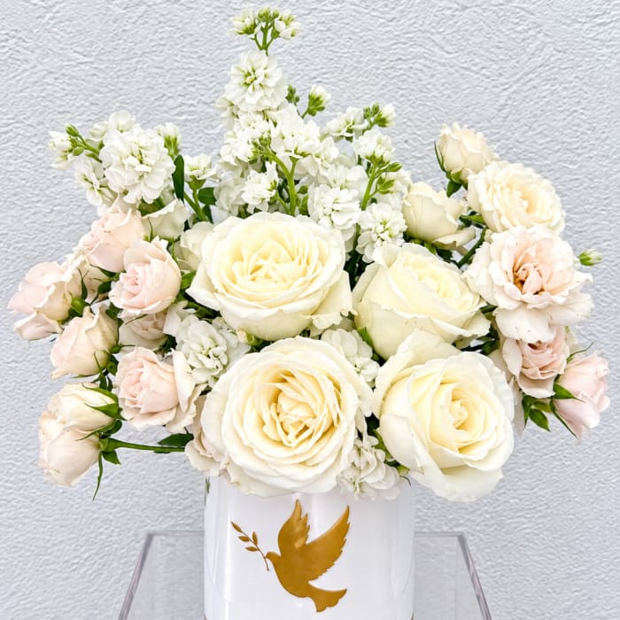 White and blush roses arranged in a white vase with a gold dove emblem