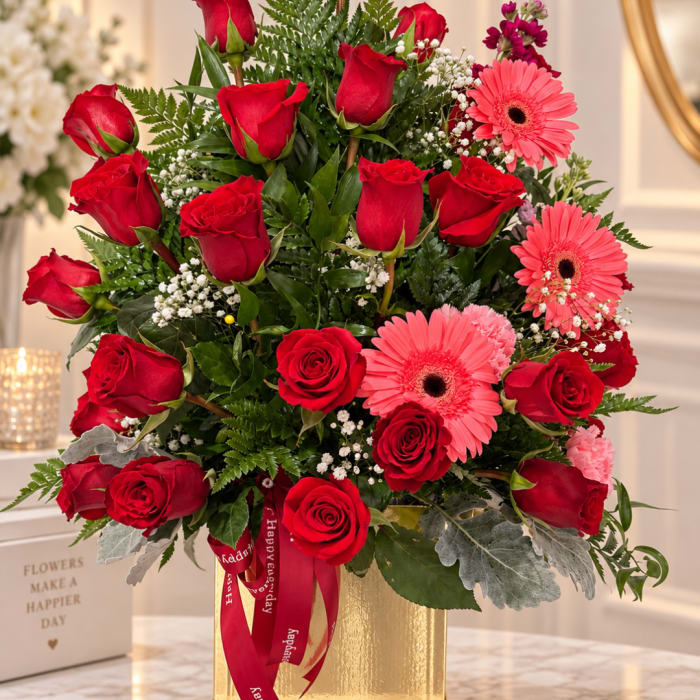 Red roses and pink gerbera daisies arranged in a gold vase