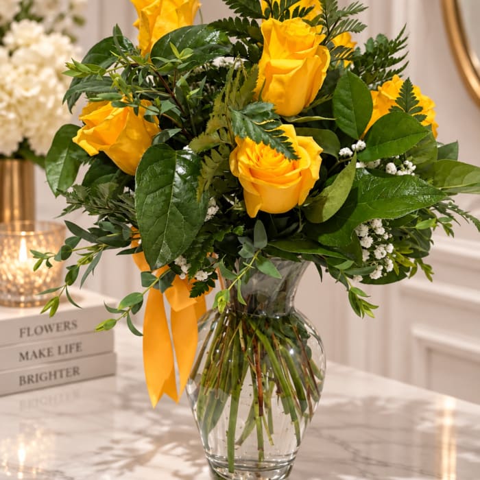 Yellow roses in a clear glass vase with a yellow ribbon