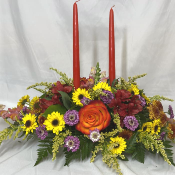 Floral centerpiece with two red taper candles and mixed blooms in a low arrangement