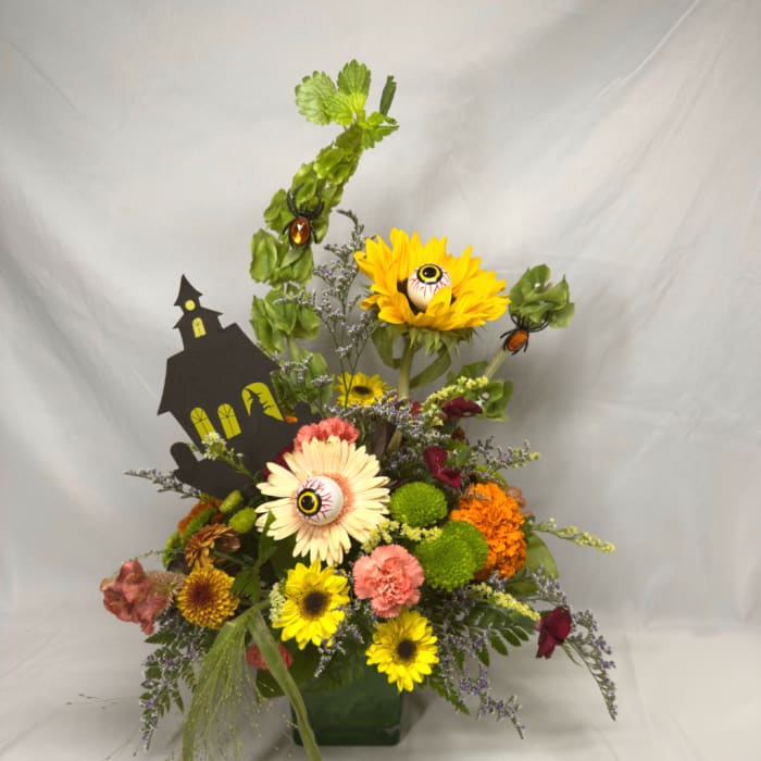 Halloween floral arrangement with sunflowers, mums, and eyeball picks in a green container