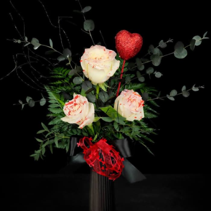 White roses with red speckles and a red heart pick in a black wrap