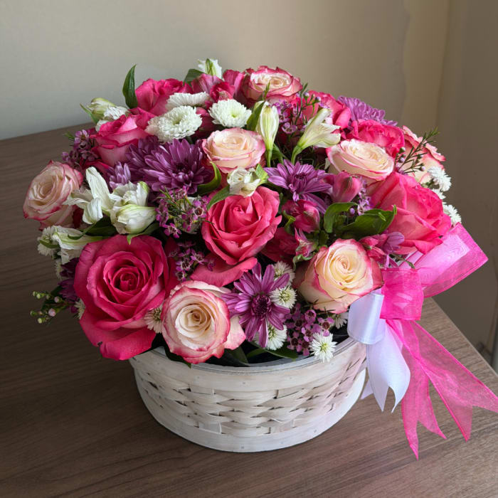 Pink and white rose bouquet in a white basket with a pink ribbon