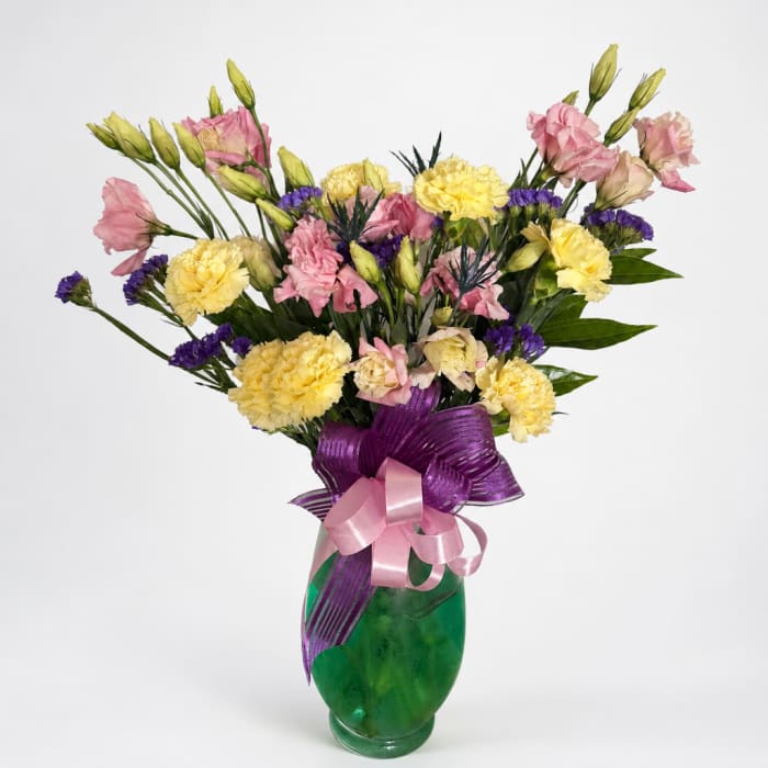 Pink and yellow mixed bouquet in a green glass vase with purple ribbon