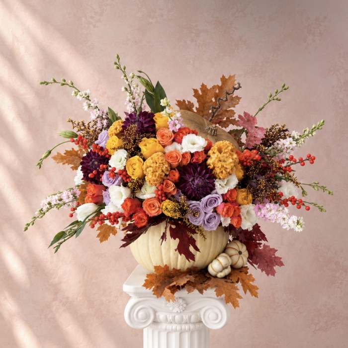 Colorful floral arrangement in a pumpkin vase with autumn leaves