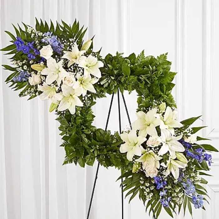 Two floral wreaths on black stands with white lilies and blue flowers