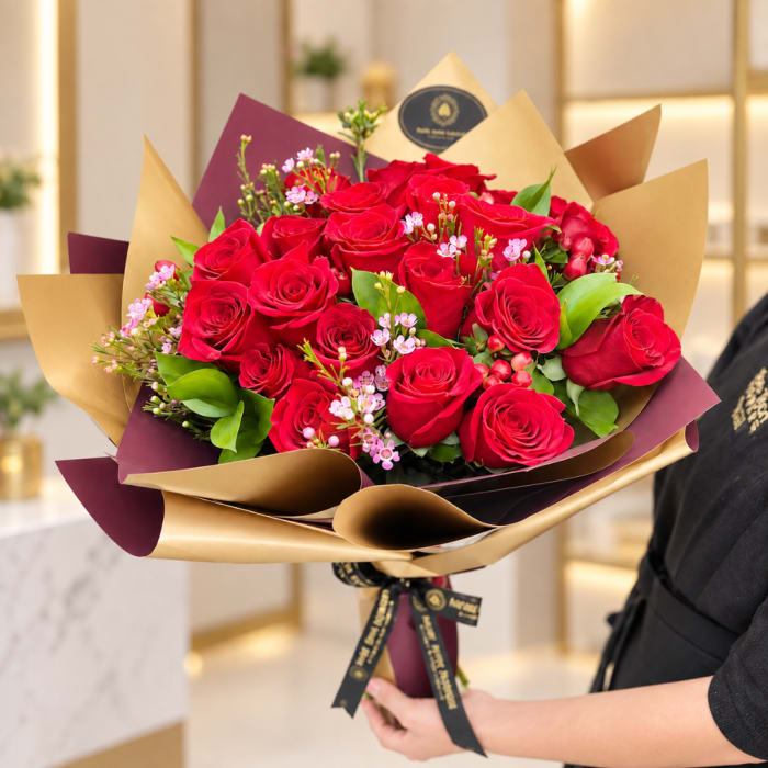 Handheld bouquet of red roses with pink filler flowers in gold and burgundy wrap