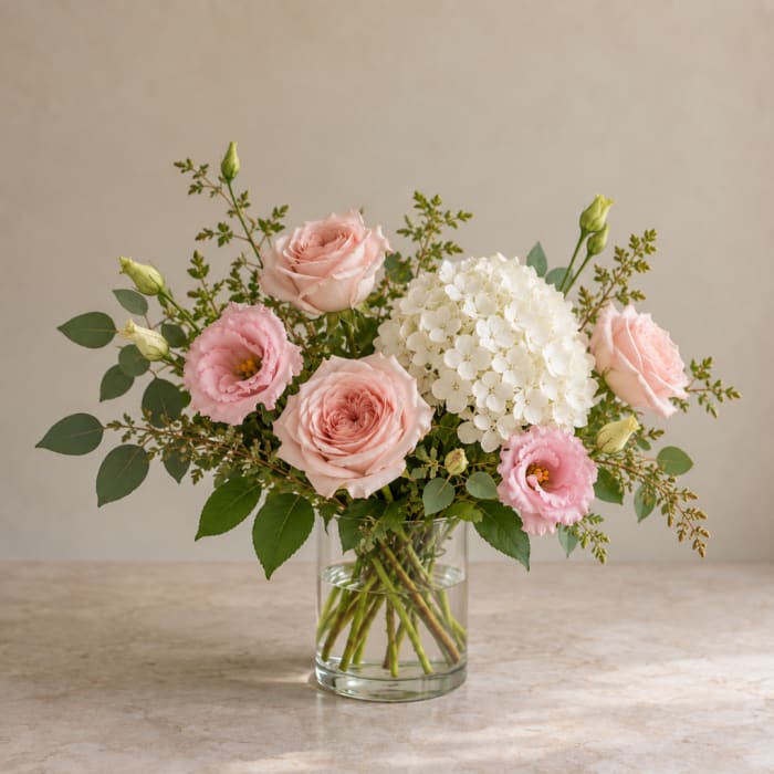 Pink roses and lisianthus with white hydrangea in a clear glass vase