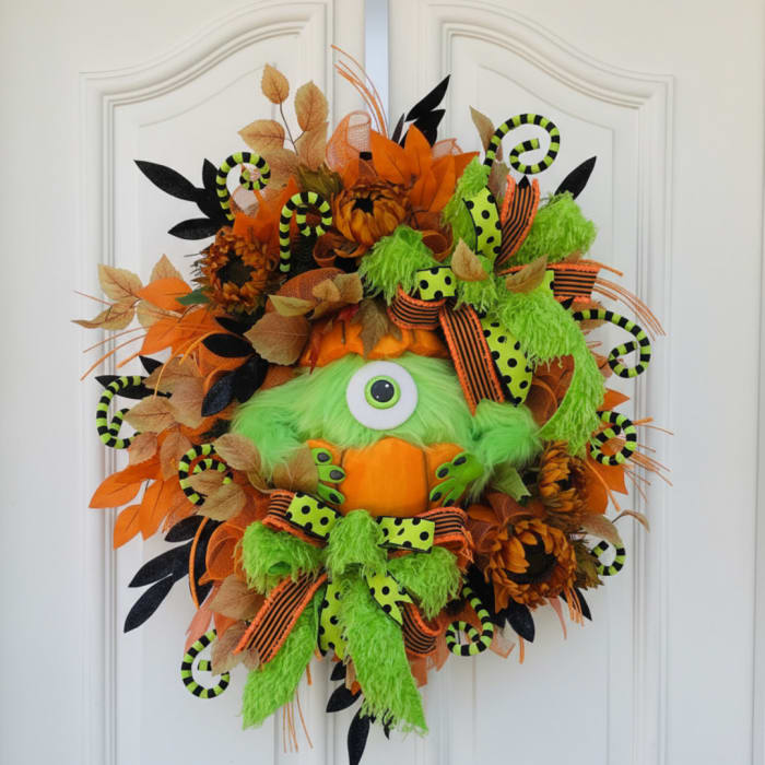 Halloween wreath with a green one-eyed monster face and orange accents