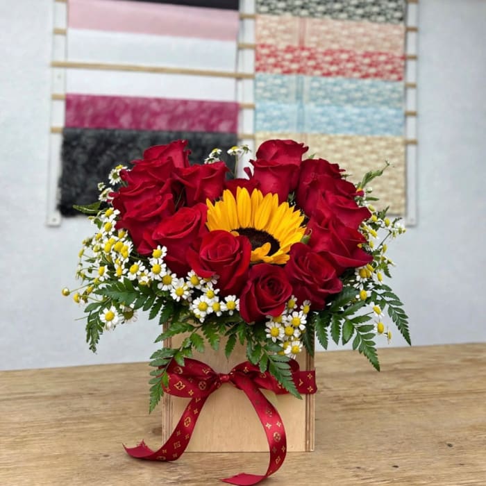 Red roses and a yellow sunflower in a wooden box with a red ribbon