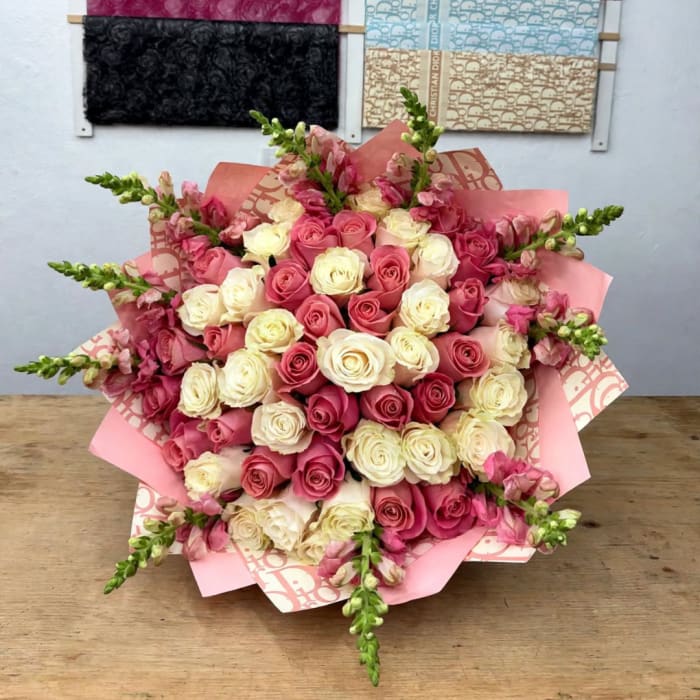 Bouquet of pink and cream roses with pink snapdragons wrapped in pink paper