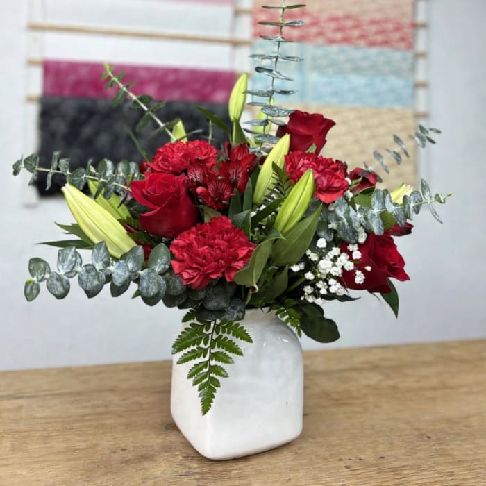 Red roses and carnations in a white vase with lilies and eucalyptus