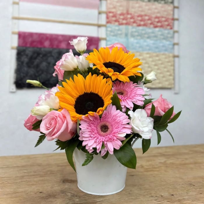 Pink and white flowers with sunflowers in a white bucket vase
